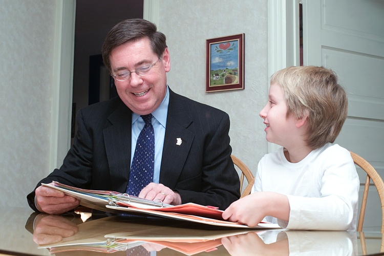 Young child sharing project materials with state senator at her dining room table. Both are smiling in the moment of engagement apparently having a good time together.