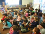 Kindergarten class listening as they sit together on the classroom floor.