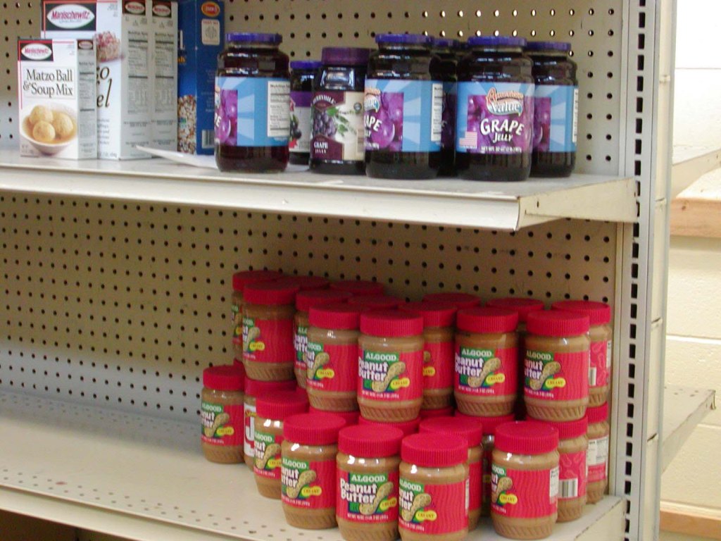 Food bank shelves with just some jars of peanut butte and jelly and empty shelves.